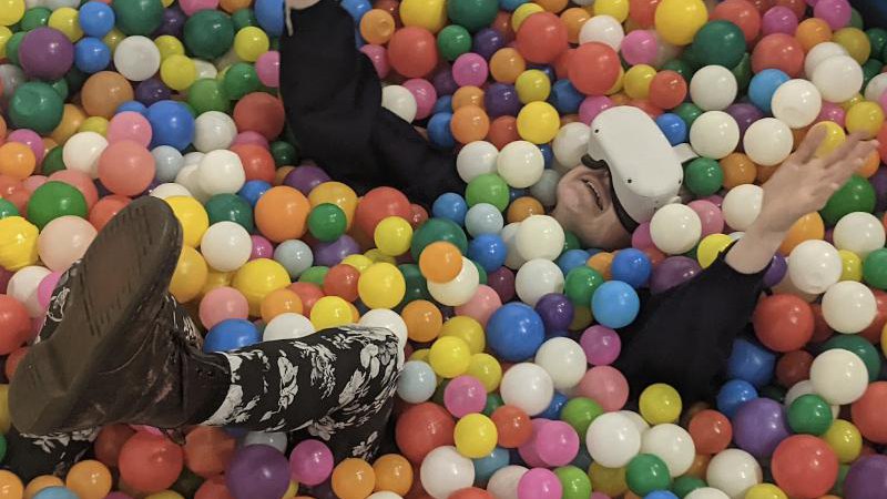 Visitor in a VR headset lying in a ball pit